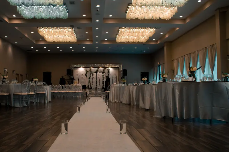 Ballroom set for a wedding reception with chandeliers and a white aisle runner
