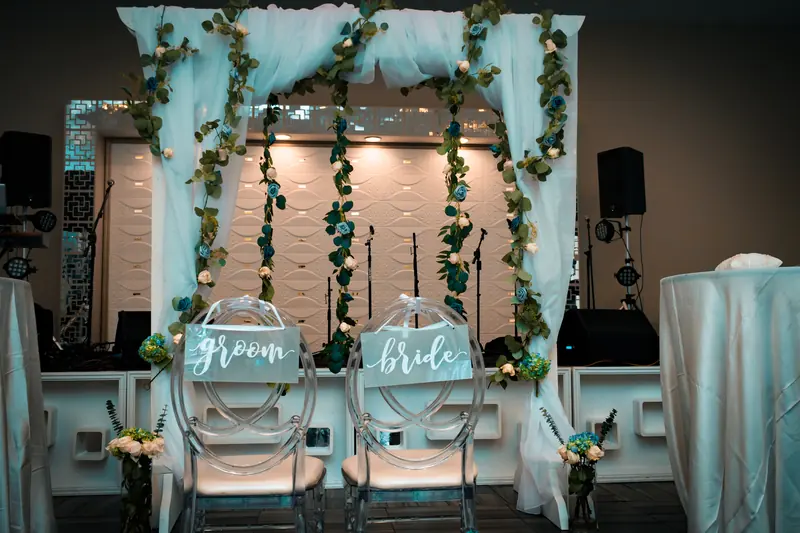Bride and groom chairs under a draped arch with greenery at a ballroom wedding