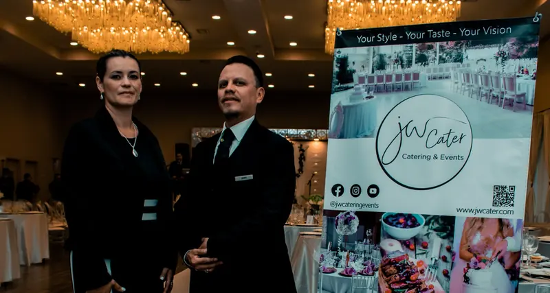 Johana and John William Godoy in a ballroom with the JW Cater banner