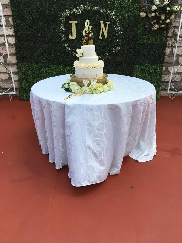 Wedding cake under a greenery wall with the couple's initials