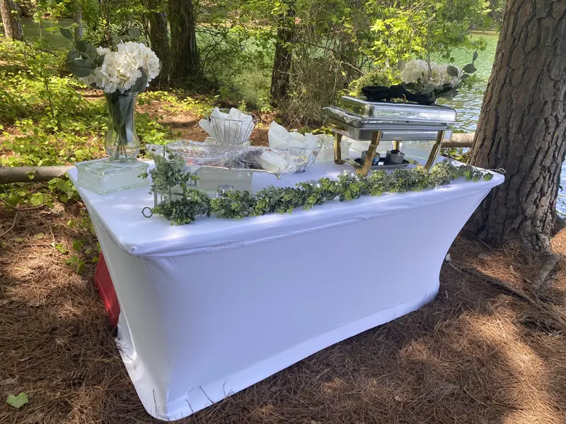 Outdoor buffet with chafers and white flowers by the lake