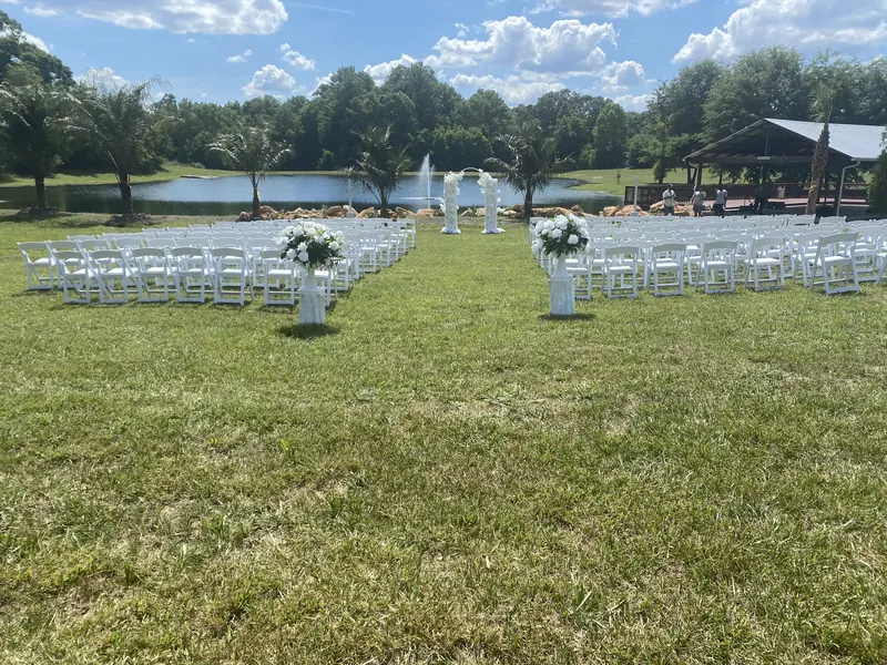Outdoor ceremony with white chairs and floral pillars facing a lake