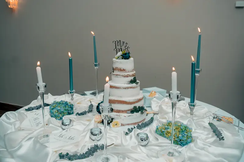 Three-tier semi-naked wedding cake with blue flowers and teal candles