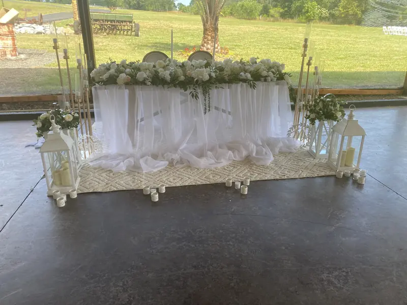 Head table with white draping, roses and lanterns under a pavilion
