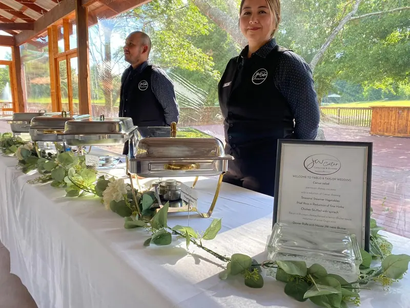 JW Cater staff behind a buffet line with a framed menu