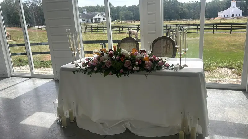 Sweetheart table with a floral garland and candles, windows facing a horse farm
