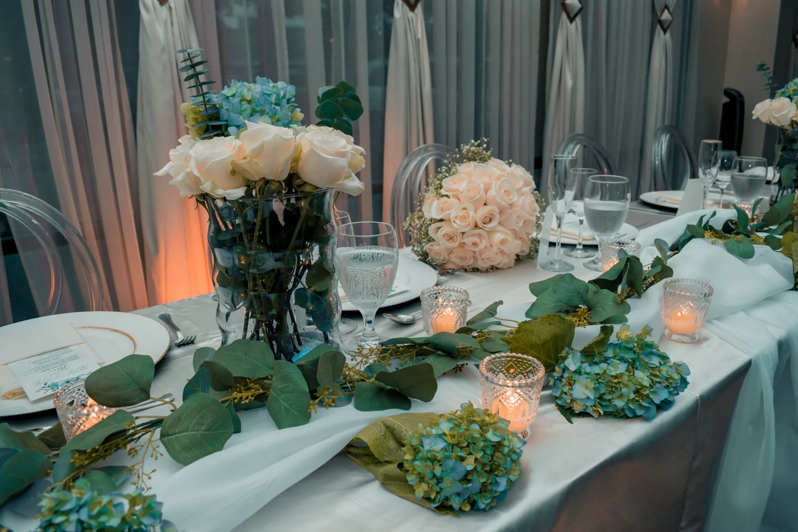 Wedding head table with white roses, blue hydrangeas, eucalyptus and candlelight set by JW Cater