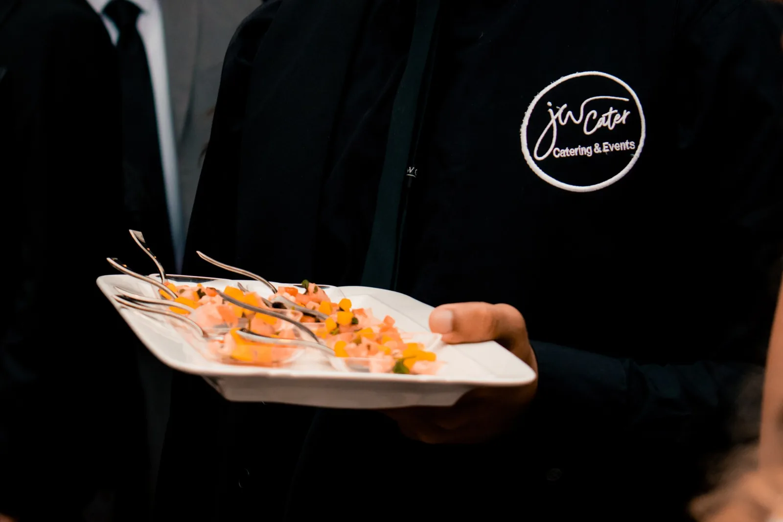 JW Cater server holding a plate of passed appetizers