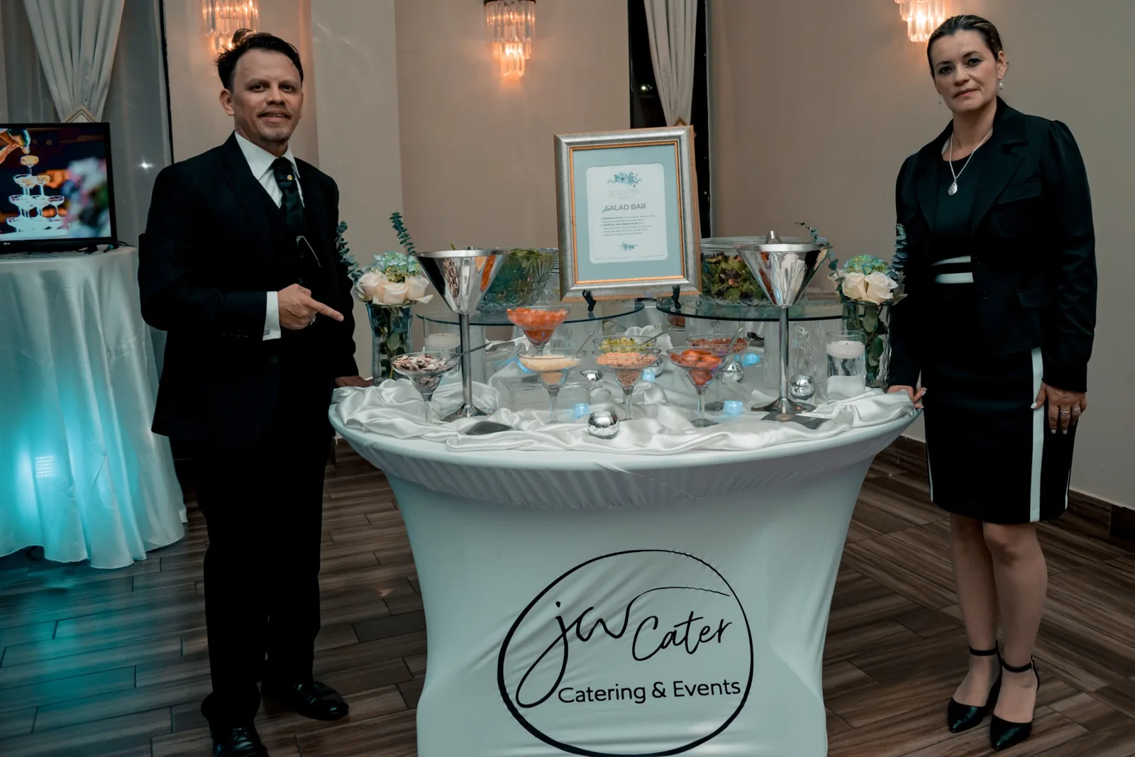John William and Johana Godoy, founders of JW Cater, beside their salad bar station with the JW Cater logo at a wedding