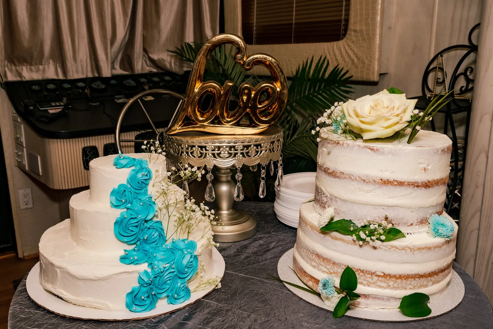 Two wedding cakes, one with teal rosettes, under a gold love sign