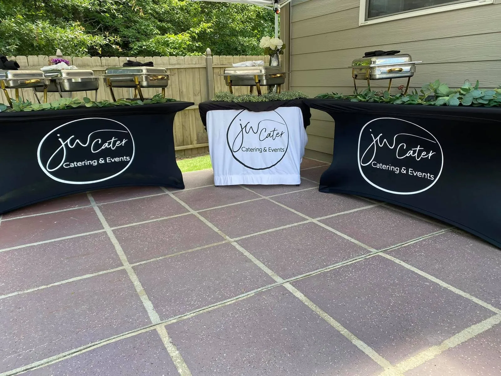 Three buffet tables with JW Cater covers on a backyard patio